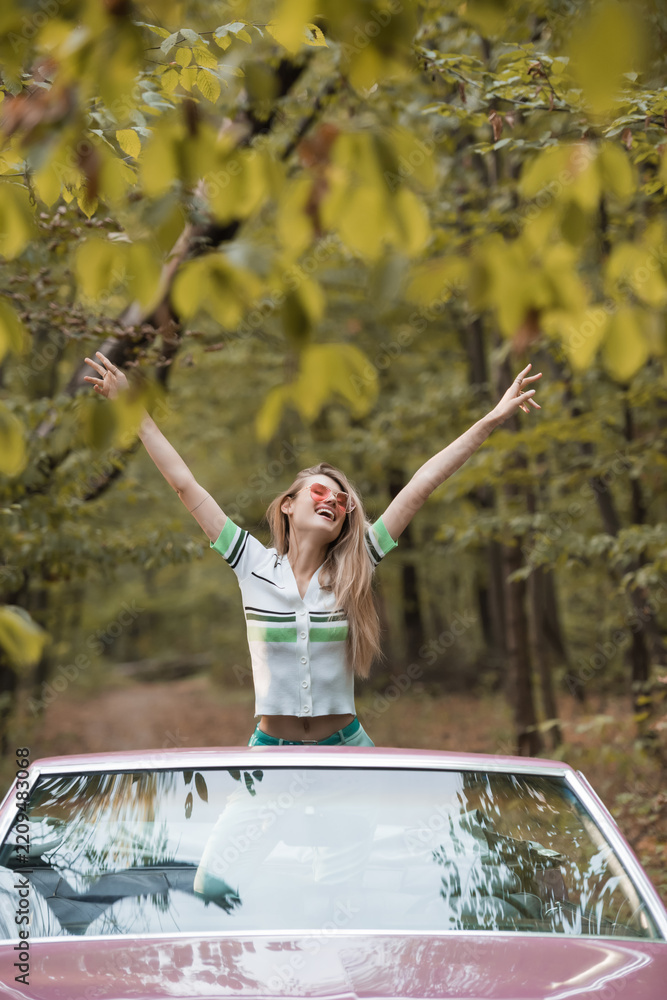 Obraz premium Joyful road trip adventure of happy woman in a pink vintage convertible through autumn foliage