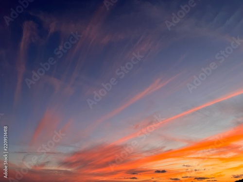 Dramatic sunset sky with bright orange and pink cirrus clouds streaks
