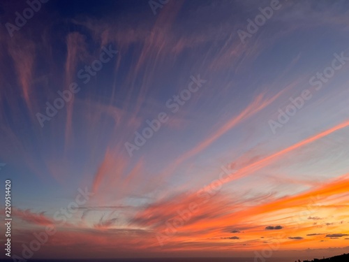 Dramatic sunset sky with bright orange and pink cirrus clouds streaks
