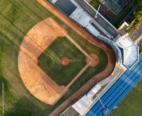 Aerial view of a baseball field with a dirt infield and green grass outfield, adjacent to a running track in Santo Domingo, Distrito Nacional, Dominican Republic.