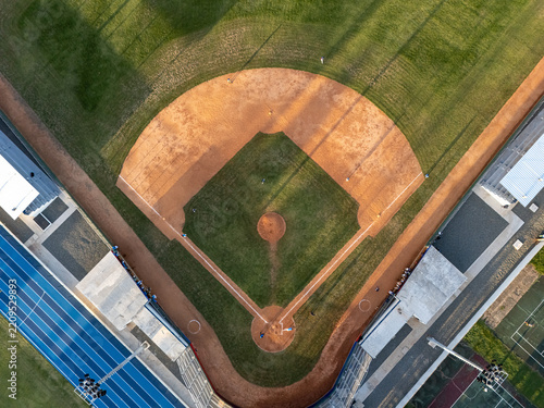 Aerial view of a baseball field with a dirt infield and green outfield grass, featuring stadium lights and adjacent blue running track in Santo Domingo, Distrito Nacional, Dominican Republic.