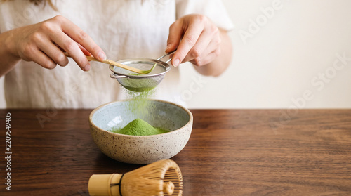 Fotografie Matcha powder passes through a metal sieve into a rustic bowl to ensure a smooth and lump-free texture