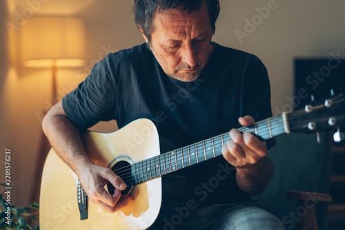 Man playing an acoustic guitar at home, close-up of hands strumming and fretting the strings, hobby and music concept in a cozy warm interior.
