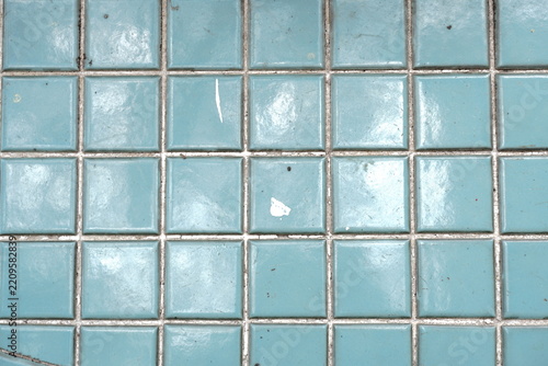 Glossy square teal tiles with thin grey grout lines some showing minor wear and imperfections