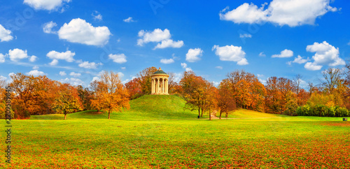 Autumn landscape - view of the Englischer Garten public park with circular colonnade on the hill, Munich, Bavaria, Germany