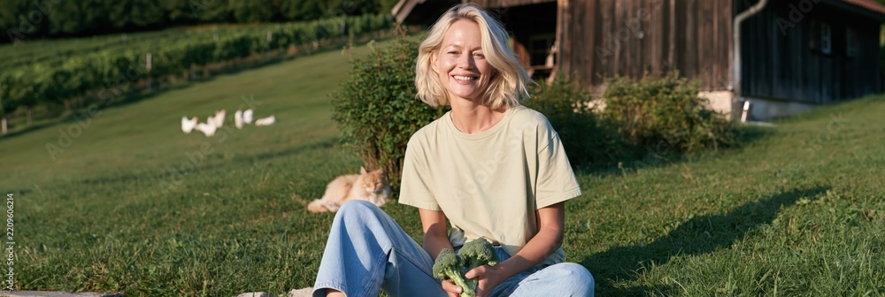 Fototapeta premium Woman sitting on a sunny hillside holding fresh vegetables for rural farm lifestyle background and sustainable living banner