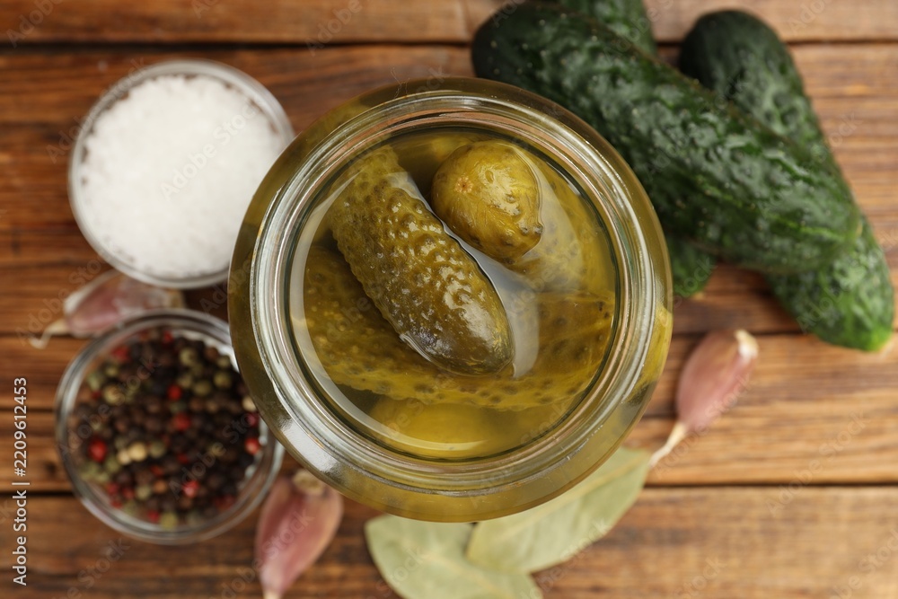 Fototapeta premium Pickled cucumbers in glass jar, fresh vegetables and spices on wooden table, flat lay