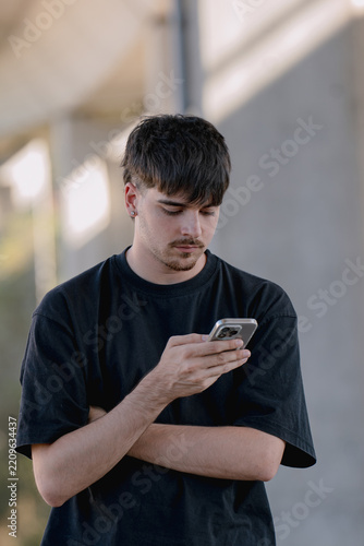 Young Caucasian man focused on smartphone, serious expression, using mobile phone outdoors, texting and browsing online