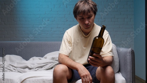 Obraz na plátně Man with an unhealthy appearance and messy hair sitting on a bed in a messy room
