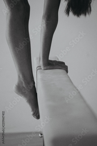 Monochrome photograph of female diver gripping low diving board edge, legs and arms poised above pool while preparing to jump into water