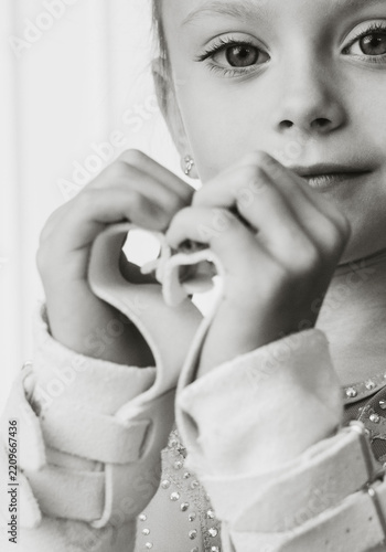 Close-up portrait of young girl forming heart gesture with hands while wearing medical arm brace in monochrome lighting