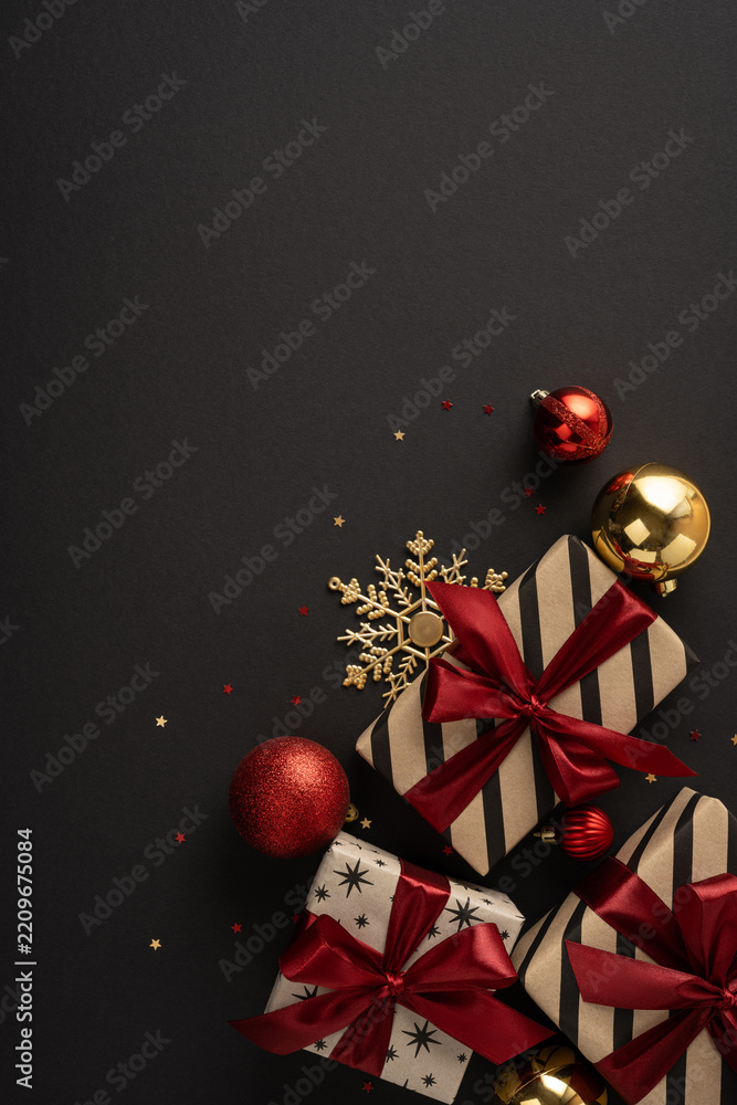 Obraz premium Merry Christmas and happy New Year gifts with red ribbons gold ornaments on vertical dark black background with space for design