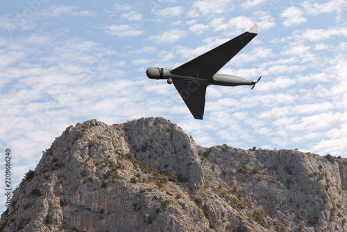 Fixed wing drone flying above rocky mountain landscape under cloudy sky