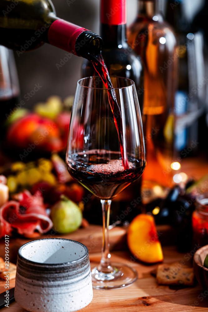 Obraz premium Pinot Noir red wine poured from bottle during lunch gathering. Authentic food pairing with rich cheese, prosciutto on table. Sommelier expertise, elegant dining culture and social connection.
