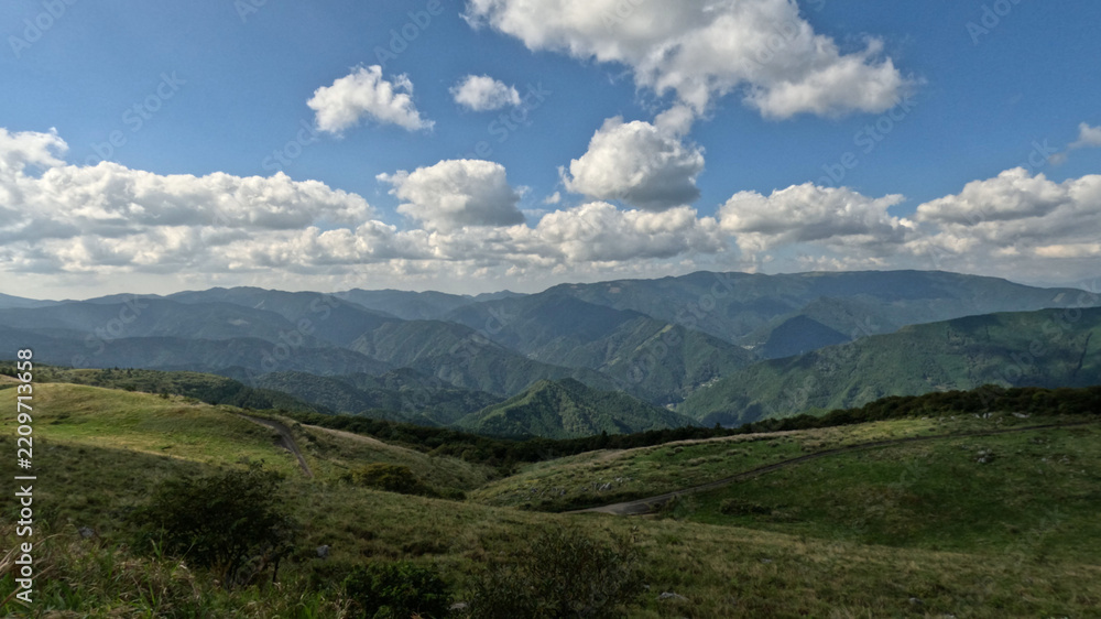 Fototapeta premium Grassy upland slopes and layered forested ranges under broken clouds