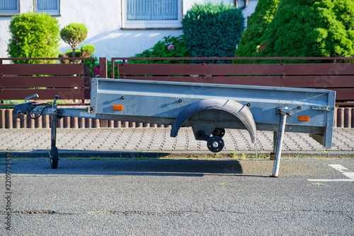 Damaged utility trailer with missing wheels parked on residential street in daylight