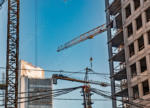 Tower cranes working on a multi-story modern residential construction site with clear blue sky