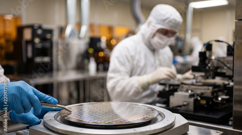 Technician handling silicon wafer in cleanroom environment for semiconductor manufacturing process
