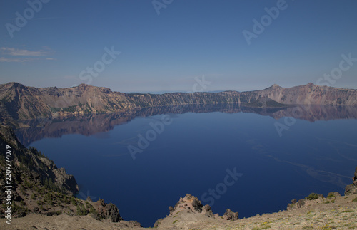 A panoramic view of deep blue Crater Lake in Oregon, reflecting clear sky against rugged volcanic mountains and caldera - Oregon, United States