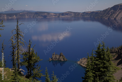 Phantom Ship rock formation rises from the deep blue waters of Crater Lake in a calm and majestic mountain environment - Oregon, United States