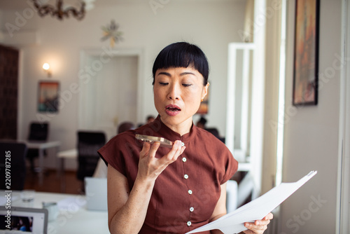 Woman dictating into smartphone while holding documents