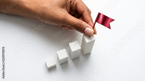 Hand placing red flag on top of rising white bar chart representing success