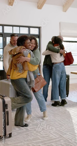 Vertical video: Diverse friends coming in entry area hugging placing luggage laughing and reuniting