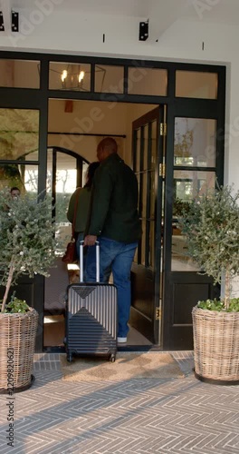Vertical video: Arriving, African American couple entering via black glass door into foyer
