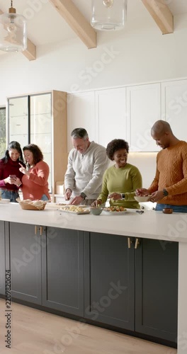 Vertical video: Family cooking at island with two women arriving and checking phone for dinner