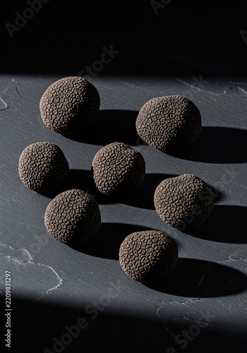 Whole raw black truffles scattered on a dark textured surface with copy space. Dramatic shadows and natural lighting create a moody feel, food, gastronomy, culinary