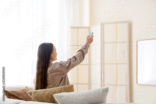Energy efficiency and climate control, woman using air conditioner remote at ...