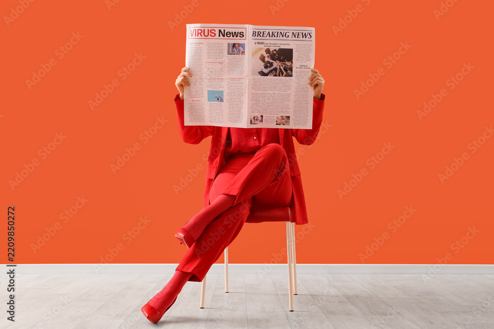 Fototapeta premium Pandemic news and health crisis, woman in red suit reading newspaper about virus updates and breaking news while sitting on chair against orange background