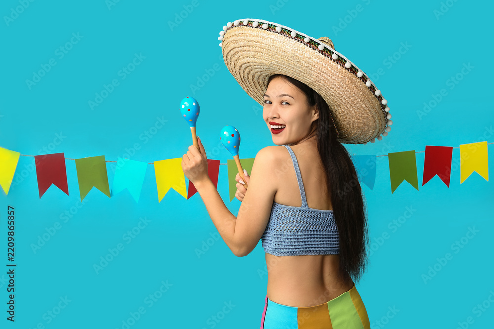 Obraz premium Cinco de mayo celebration and mexican culture, happy young woman wearing a sombrero and holding maracas with festive party flags on blue background