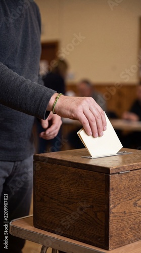Casting a Vote: A close-up shot captures a person's hand inserting a ballot into a wooden ballot box, symbolizing the democratic process and civic duty.