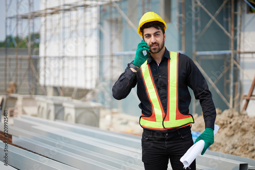 Worker wearing holding blueprint while talking on smartphone at a construction site