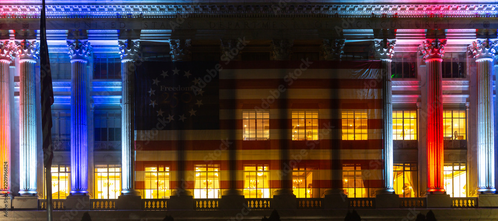 Obraz premium American flag across government building. American freedom banner on facade. Illuminated columns frame American celebration. July fourth honors American independence.