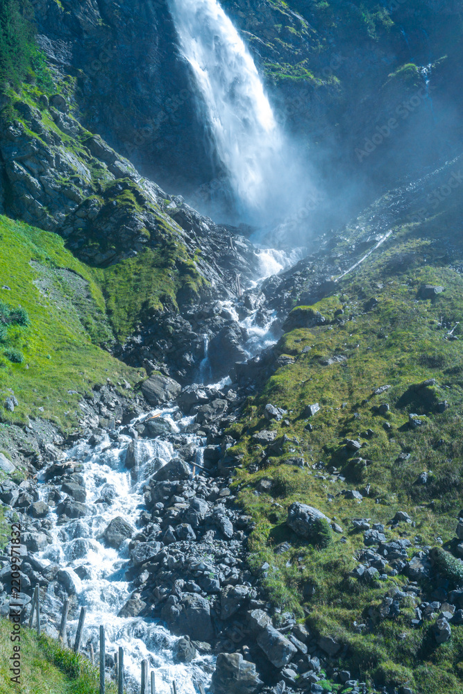Obraz premium Waterfall flows across Swiss mountain landscape. Waterfall forms a natural Swiss landmark. Switzerland scenery includes waterfall among mountains. Alpine nature frames waterfall near rocks.