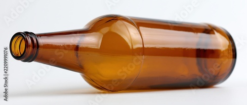 Empty amber glass beer bottle lying on its side on white background
