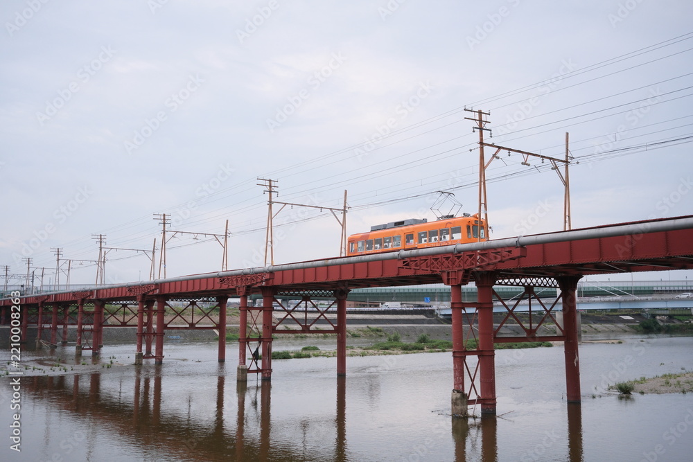 Fototapeta premium OSAKA, JAPAN - SEPTEMBER 2026: An electric tram crossing an old iron bridge over the Yamato River in Osaka.