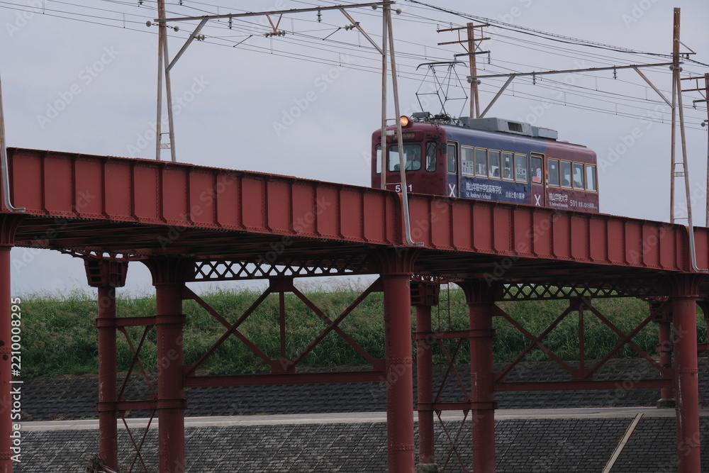 Obraz premium OSAKA, JAPAN - SEPTEMBER 2026: An electric tram crossing an old iron bridge over the Yamato River in Osaka.