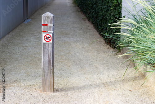 Fotografie Wooden post with no dogs allowed sign stands on a gravel pathway bordered by gre