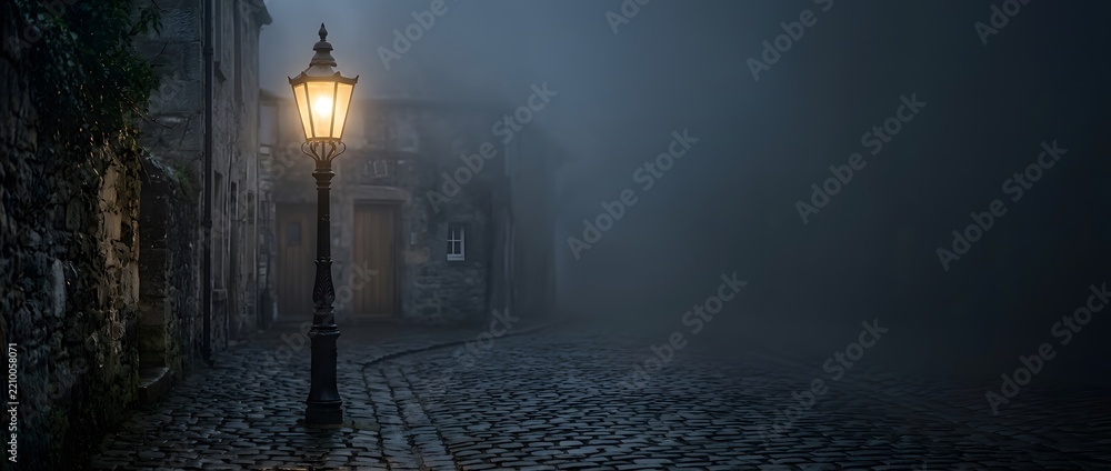 Naklejka premium Victorian cobblestone street lit by a glowing gas lamp on a foggy night.