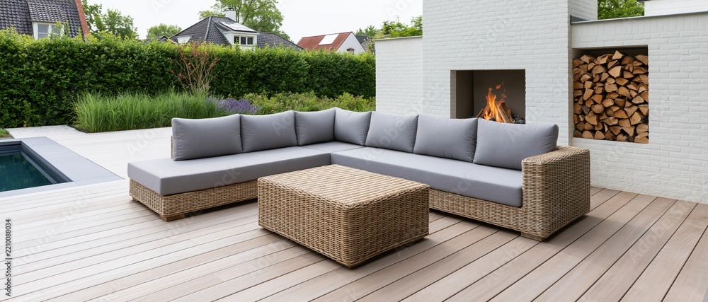 Obraz premium L-shaped wicker sectional sofa with grey cushions on a wooden deck beside a firepit and swimming pool in a suburban backyard