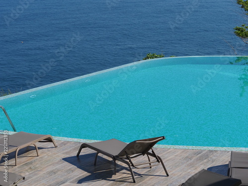 View of the infinity pool with sun loungers against the backdrop of the sea, and the hotel grounds.