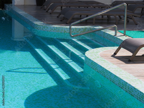 View of the infinity pool with sun loungers against the backdrop of the sea, and the hotel grounds.