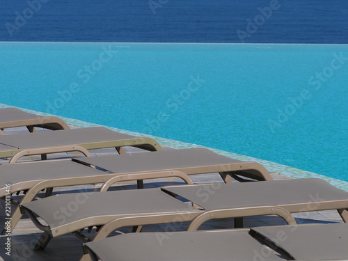 View of the infinity pool with sun loungers against the backdrop of the sea, and the hotel grounds.