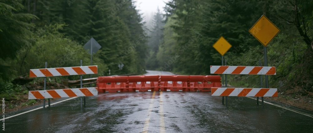 Obraz premium Road closure barricades blocking a wet two-lane highway in a forested area