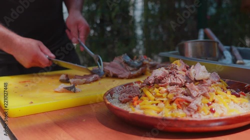 Chef adds boiled meat to Uzbek plov served on a wooden lagan, close-up