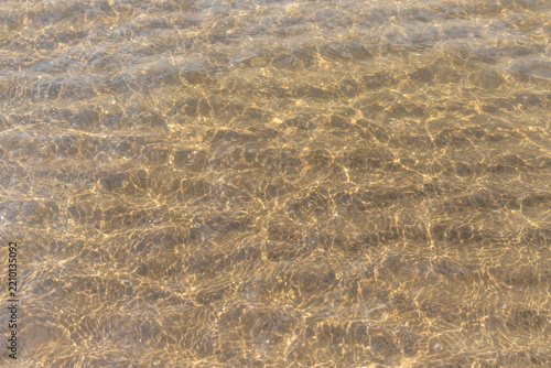 Golden sunlight on shallow beach water with rippled sand and sparkling reflec...