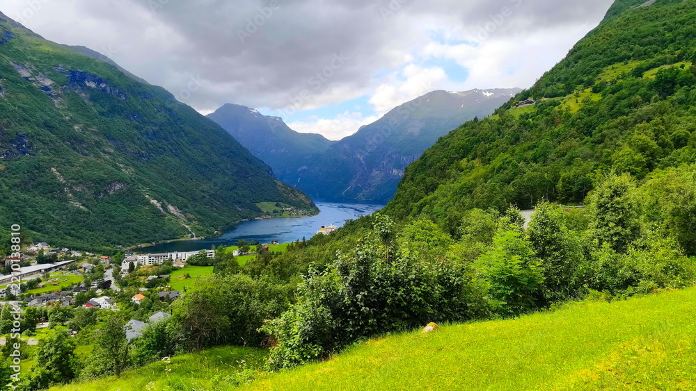 Obraz premium Scenic view of Geirangerfjord in Norway with green mountain slopes and dramatic sky, natural landscape